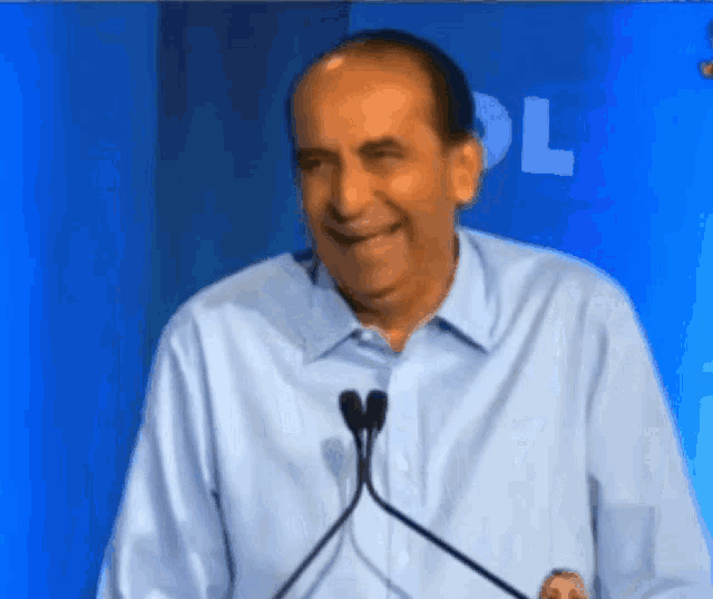 a man in a blue shirt is smiling in front of a microphone with the letter l behind him