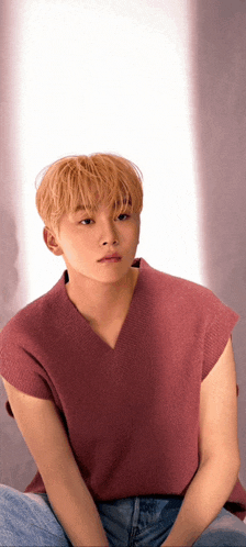 a young man with blonde hair is wearing a pink shirt and jeans