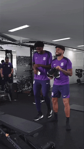 two soccer players in purple uniforms are standing in a gym with the words timão reapresen above them