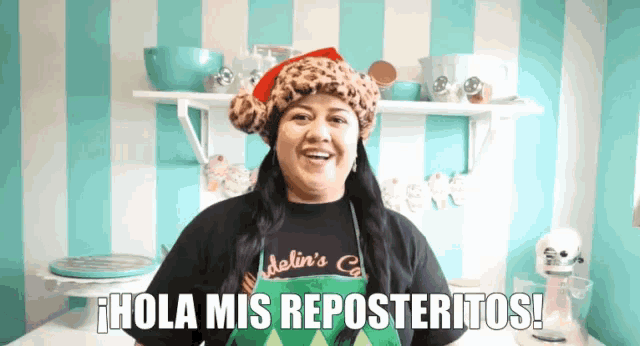 a woman wearing a santa hat and an apron says " hola mis reposteritos "