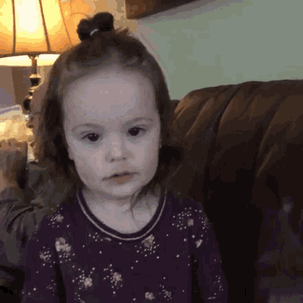 a little girl is sitting on a couch and looking at the camera