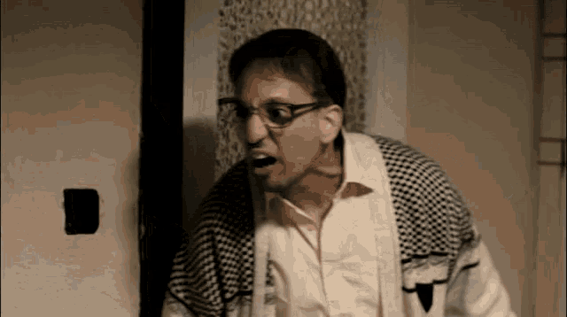 a man wearing glasses and a plaid sweater is standing in front of a door