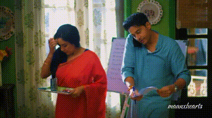 a man and a woman are standing next to each other in a room . the woman is wearing a red saree .