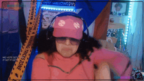a woman wearing headphones and a pink hat is standing in front of a warning tape that says halloween