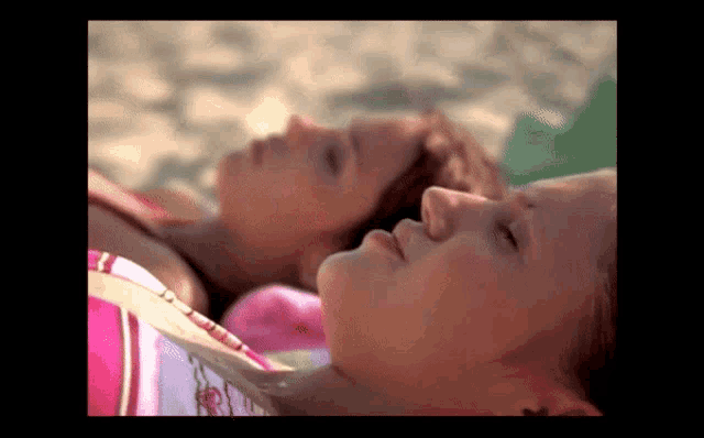 two girls are laying on the beach with their eyes closed