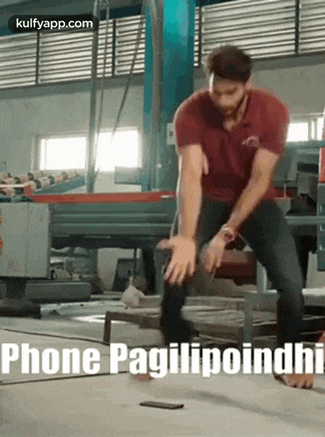 a man in a red shirt is standing on a concrete floor with a cell phone in front of him .