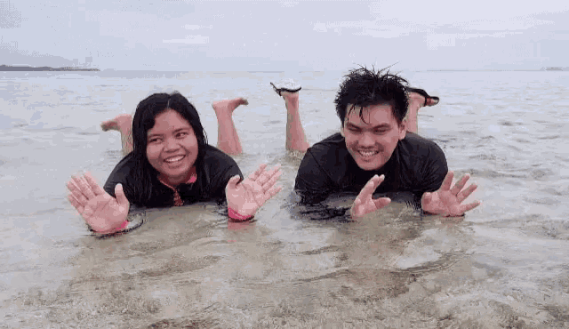 a man and a woman are laying in the ocean waving their hands