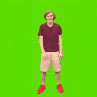 a man in a maroon shirt and khaki shorts is dancing in front of a green screen .