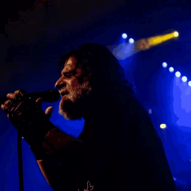a man with a beard is singing into a microphone in the dark