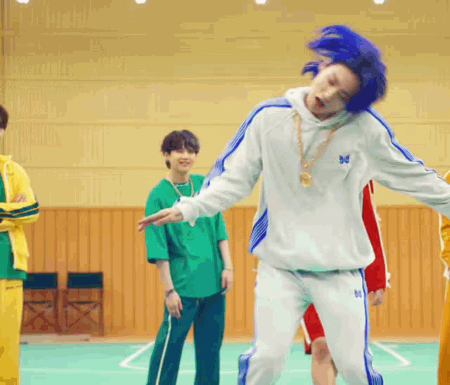 a man with blue hair and a butterfly necklace is dancing in a gym