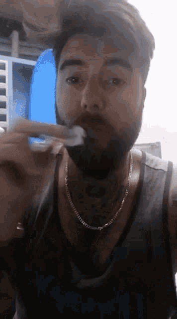 a man with a beard is brushing his teeth while wearing a tank top that says reebok