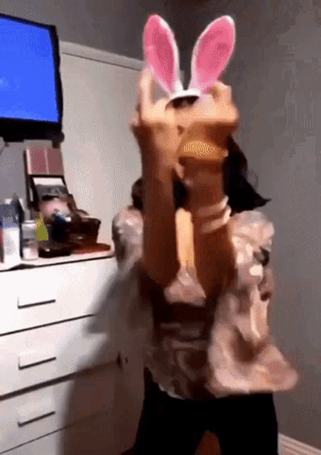 a woman wearing bunny ears is dancing in front of a television .