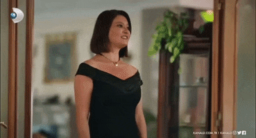 a woman in a black dress and necklace is standing in a doorway .