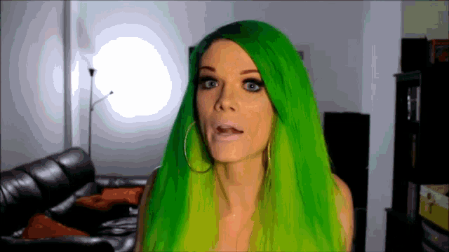 a woman with green hair and hoop earrings looks at the camera