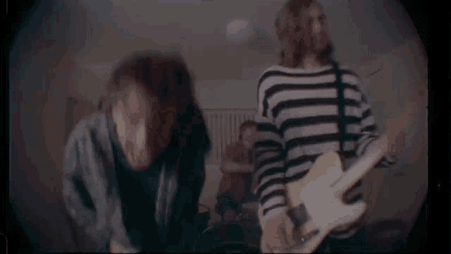 a man in a striped shirt is playing a guitar next to another man .