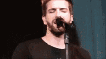 a man is singing into a microphone with his eyes closed .