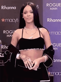 a woman is standing in front of a purple wall wearing a black crop top and a black jacket .