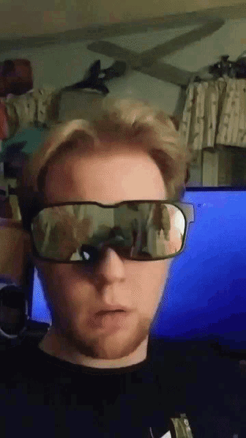a man wearing sunglasses with a reflection of a person behind him
