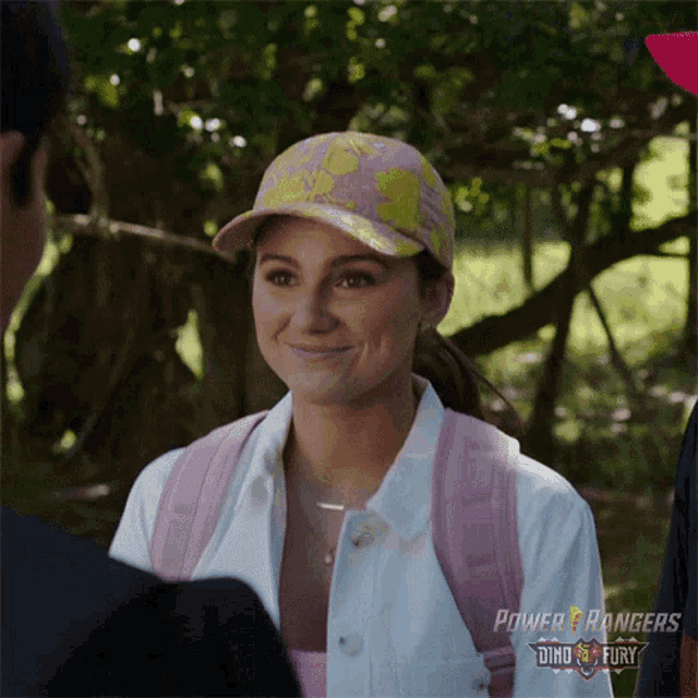 a woman wearing a pink backpack and a power rangers hat smiles at a man