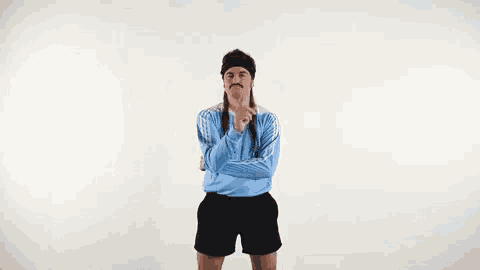 a man wearing a blue shirt and black shorts is standing with his arms crossed and making a funny face .