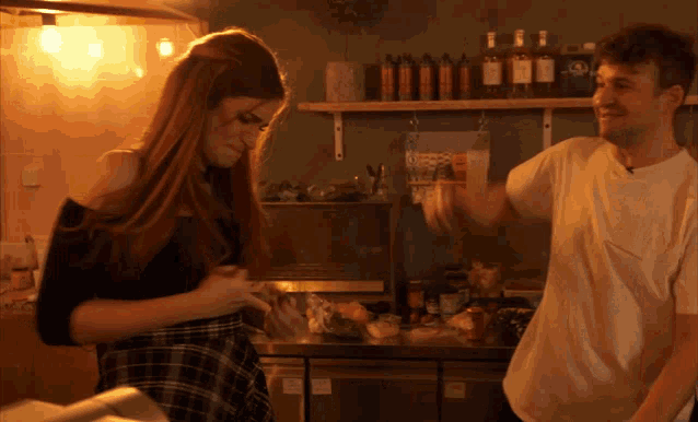 a man and a woman are dancing in a kitchen with bottles of alcohol on the shelf behind them