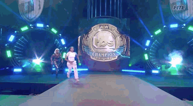two women are walking on a stage with a aew championship belt