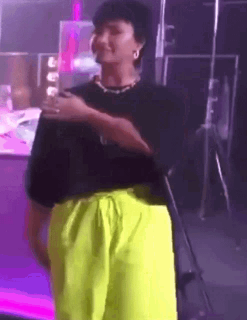 a man wearing neon yellow shorts and a black shirt is standing in a dark room .