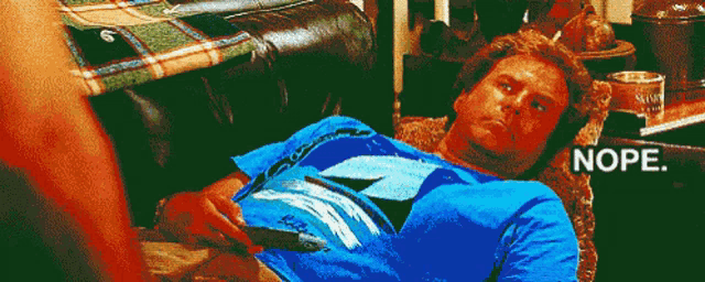a man in a blue shirt is laying on a couch with the word nope written on the bottom