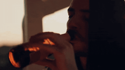 a man with long hair is drinking from a bottle .