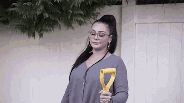 a woman wearing glasses is holding a yellow shovel in her hand .