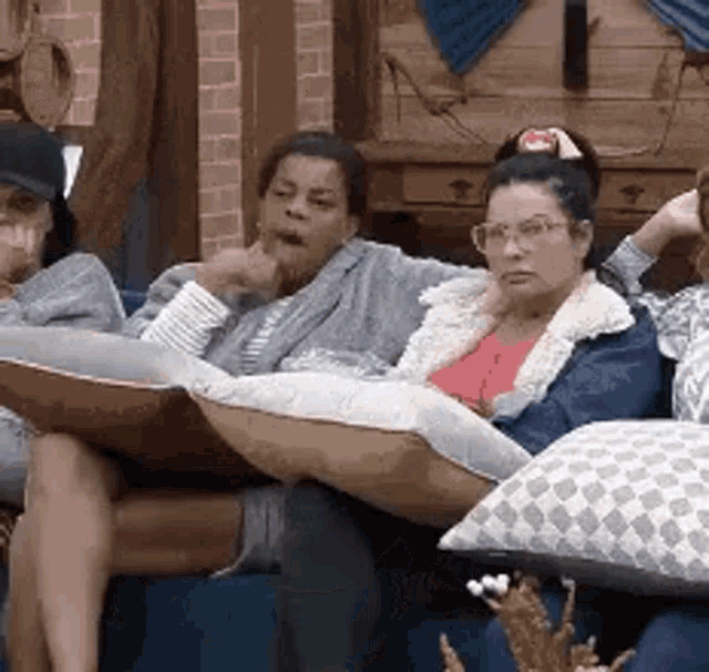 a group of people are sitting on a couch with pillows and talking to each other .