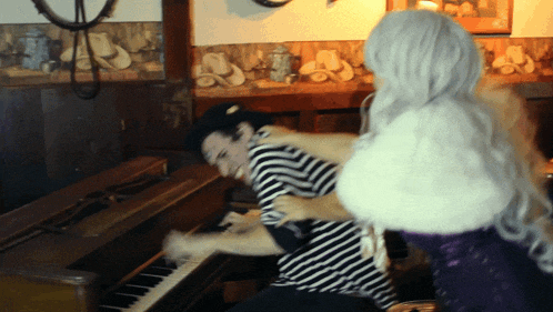 a man in a striped shirt is playing a piano while a woman holds him