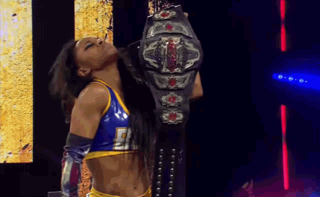 a woman in a blue and yellow outfit is holding a wrestling belt