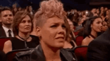 a woman with pink hair is sitting in a crowd of people at a concert and crying .