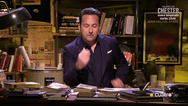 a man in a suit is sitting at a desk in front of a stack of books and a sign that says chester