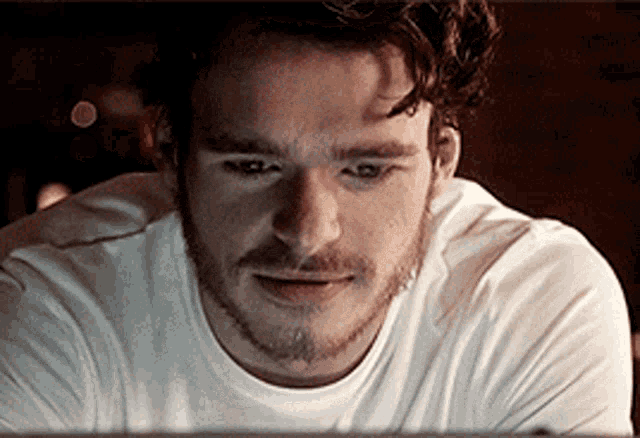 a man with a beard is wearing a white shirt and looking at something