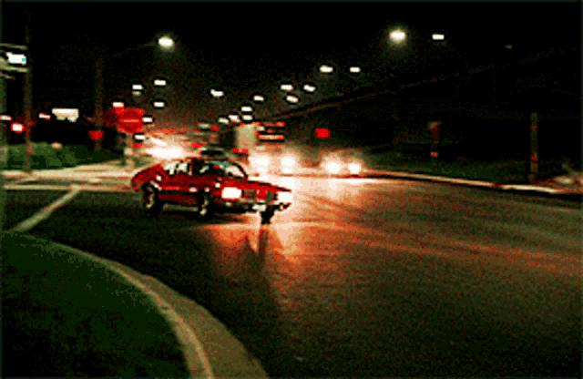 a red car is driving down a dark street