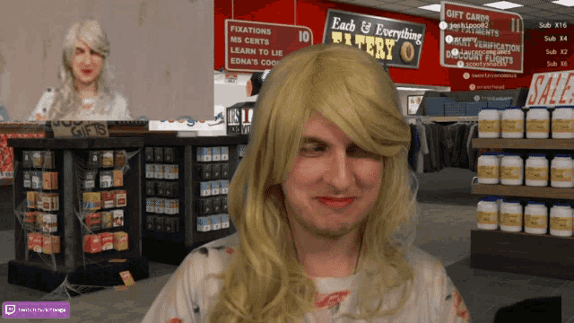 a man wearing a blonde wig stands in front of a sign that says " each & everything "