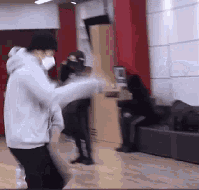 a man wearing a mask is dancing in a room while another man sits on a couch .