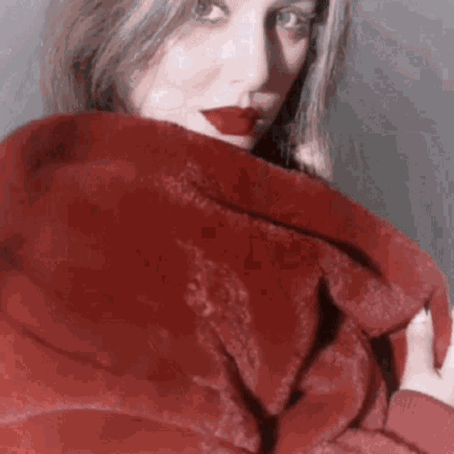a woman wearing a red fur coat and red lipstick is looking at the camera .