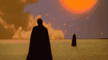 a man in a cape is standing in a desert in front of a large sun .