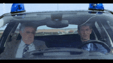 two men are sitting in a police car with a blue light on the top