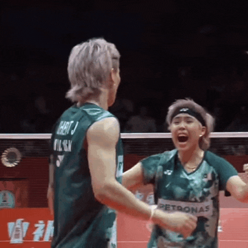 a man and a woman are playing badminton and the woman is wearing a petronas shirt