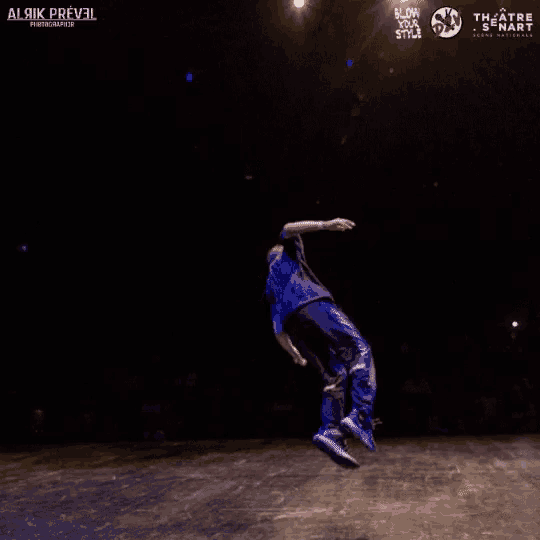 a man in a blue shirt is doing a trick on a stage in front of a sign that says " theatre & senat "