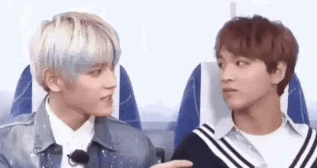 two young men are sitting next to each other on an airplane and talking to each other .