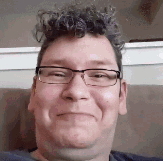 a man with curly hair wearing glasses is making a funny face .