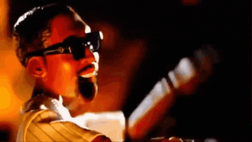 a man in sunglasses is singing into a microphone .
