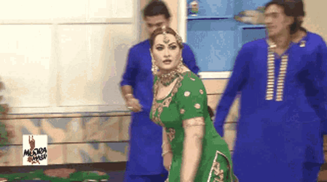 a woman in a green dress is dancing in front of men in blue