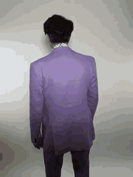 a man in a purple suit is standing in front of a wall .