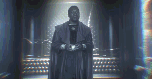 a man in a cloak is standing in a dark room holding a sword .